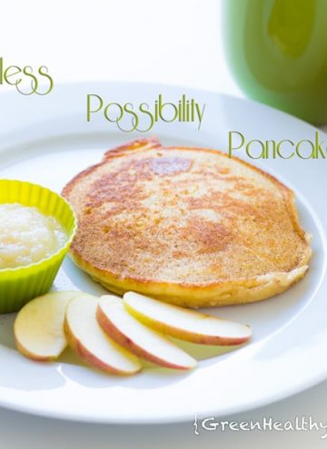 A pancake on a white plate with sliced apples and apple sauce in a small green bowl.
