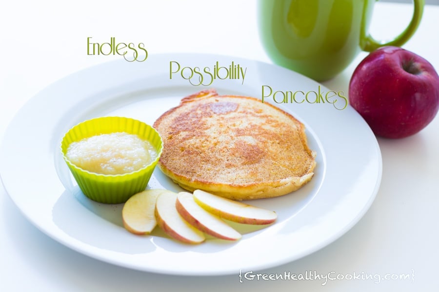 A pancake on a white plate with sliced apples and apple sauce in a small green bowl.