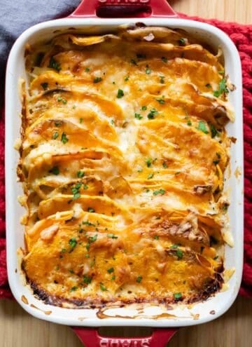 Red casserole dish with sweet potato gratin in it.
