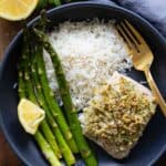 Mahi Mahi Filet with Almond Parmesan Crumble in a black bowl with white rice and asparagus on the side.