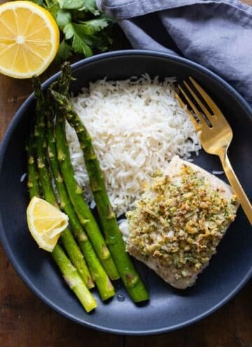 Mahi Mahi Filet with Almond Parmesan Crumble in a black bowl with white rice and asparagus on the side.