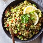 Quinoa Tabbouleh in a gray bowl on a marble surface topped with lemon slices and parsley leaves.