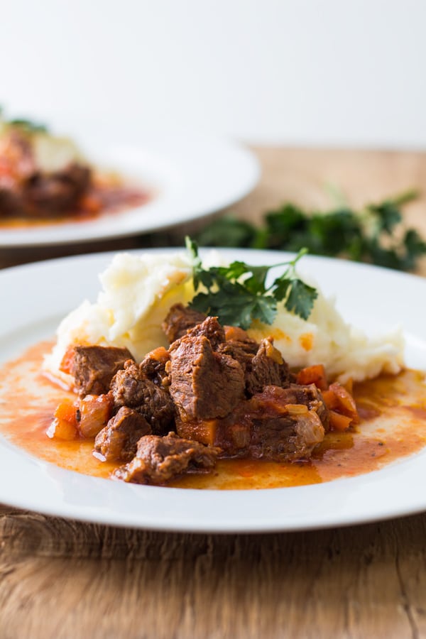 Tender Lamb Stew with Homemade Potato Mash on a white plate on a wooden table.