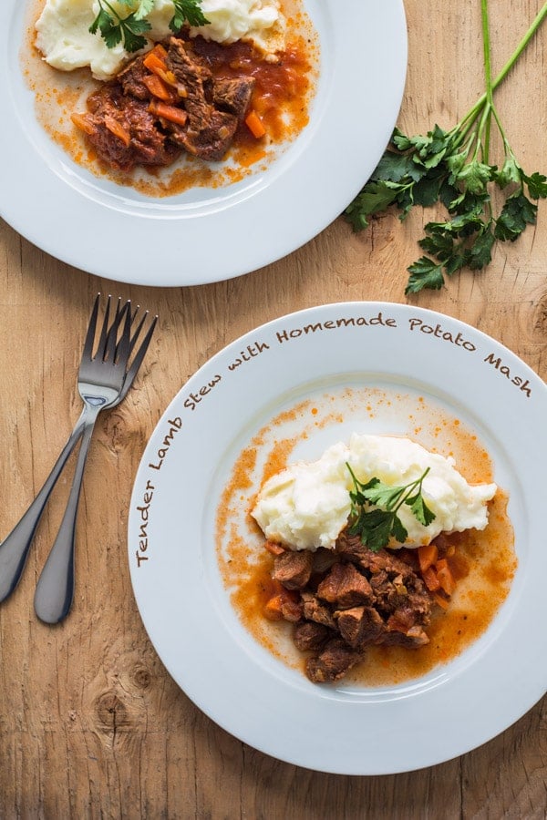 Top view of Tender Lamb Stew with Homemade Potato Mash on white plates on a wooden table with two forks, with text overlay.