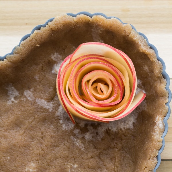 Detail of rose made with apple slices placed in heart-shaped mold with crust. 