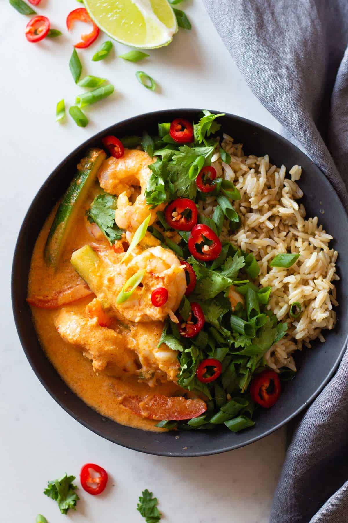 Coconut Shrimp Curry and brown rice in a grey bowl topped with herbs and chili.