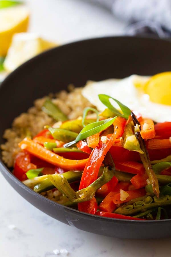 Closeup of sliced roasted vegetables in a bowl on quinoa and topped with a fried egg.