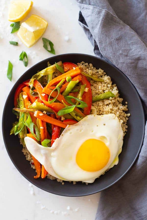 A grey bowl of quinoa, roasted vegetables, and a fried egg.