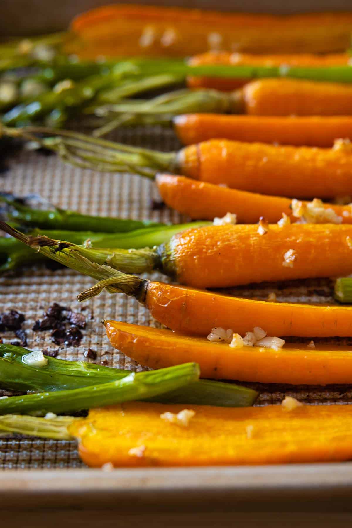 Close up of texture of roasted carrots and broccolini on a baking sheet.