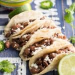 Close up of Pinto Bean Tacos with Salsa Verde on a rustic wood board with text overlay.