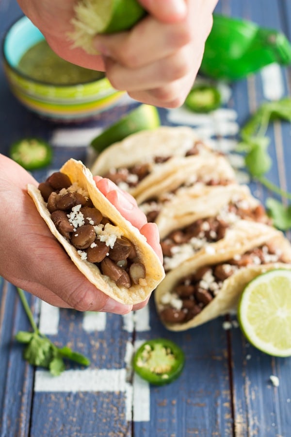 Hand holding a Pinto Bean Taco squeezing lime juice on it.