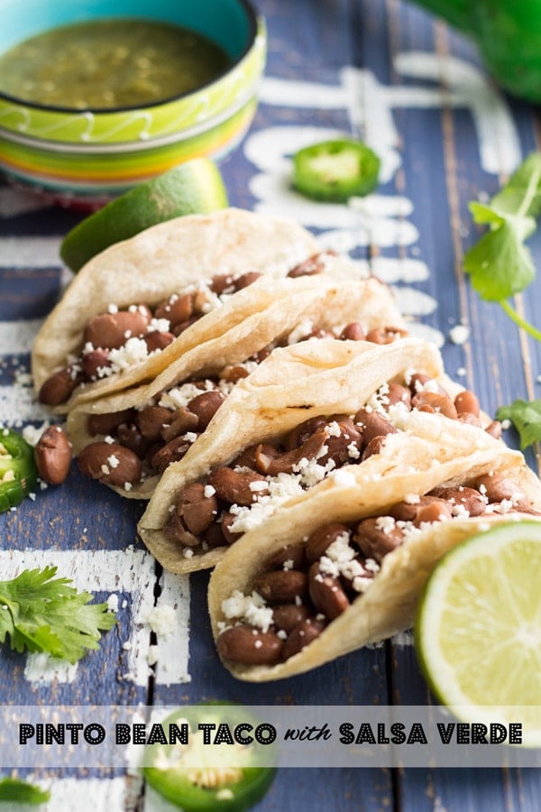 Close up of Pinto Bean Tacos with Salsa Verde on a rustic wood board with text overlay.