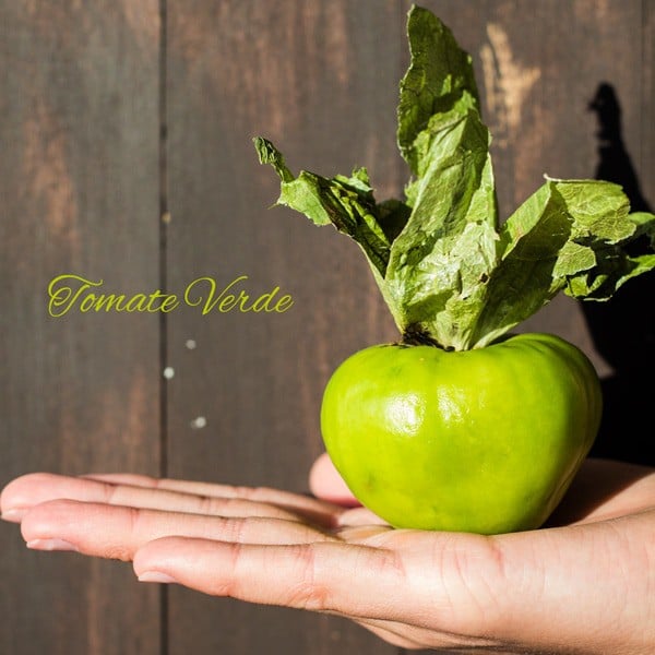 Hand holding a Tomate Verde - Tomatillo with text overlay.