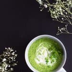 Top view of Simple Green Pea Soup on a black background with small flowers.