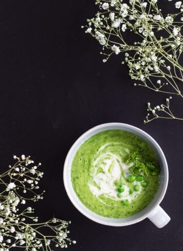 Top view of Simple Green Pea Soup on a black background with small flowers.