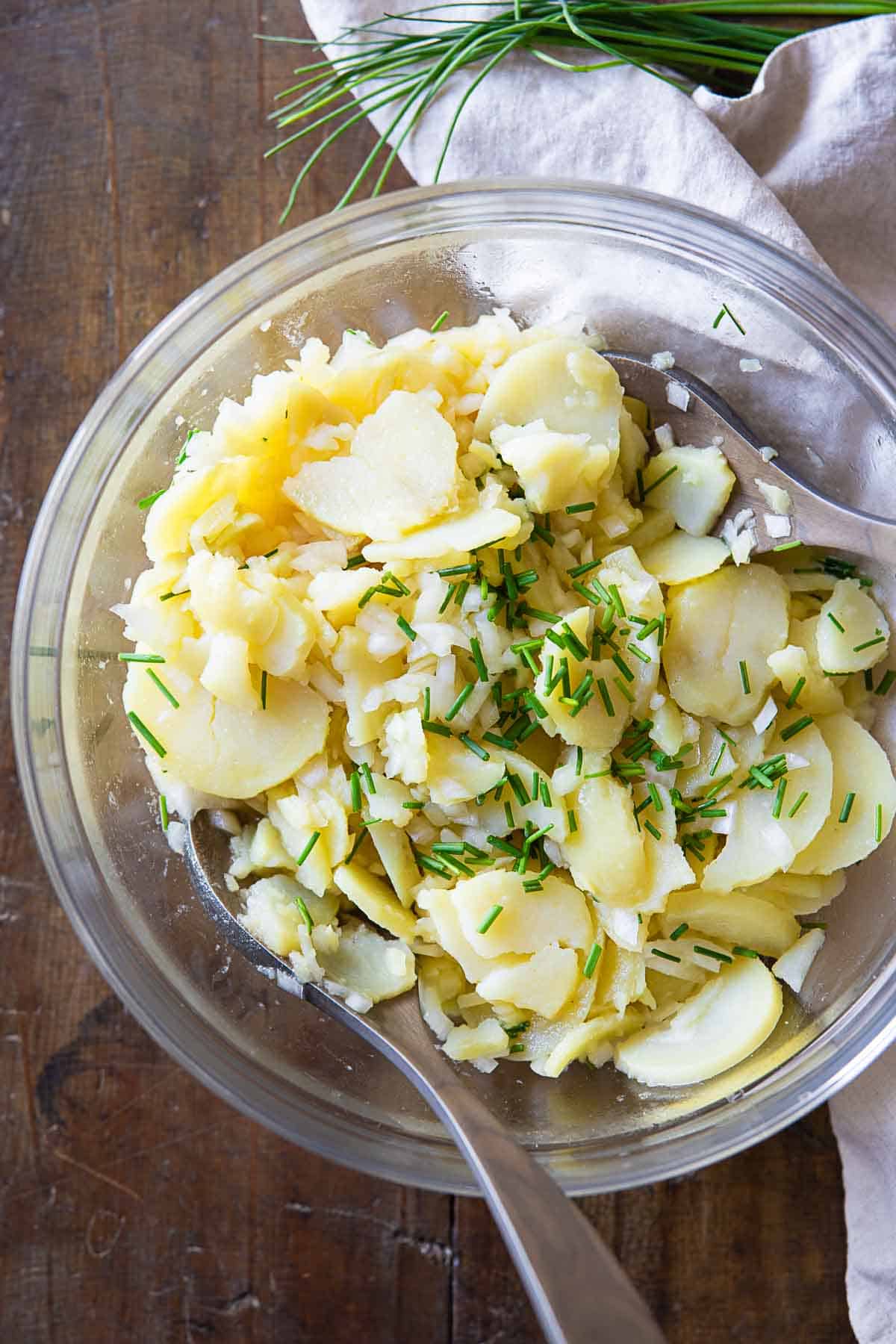 German Potato Salad in a glass salad bowl on a wooden table.