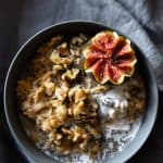 Carrot cake oatmeal in a grey bowl topped with chopped walnuts and half a fig.