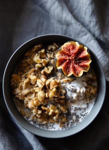 Carrot cake oatmeal in a grey bowl topped with chopped walnuts and half a fig.