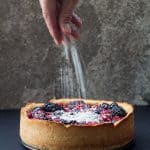 Hand sprinkling sugar on a Healthy Berry Cake.