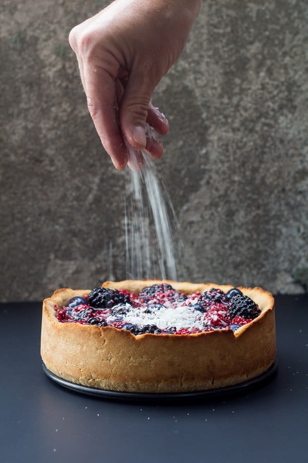 Hand sprinkling sugar on a Healthy Berry Cake.