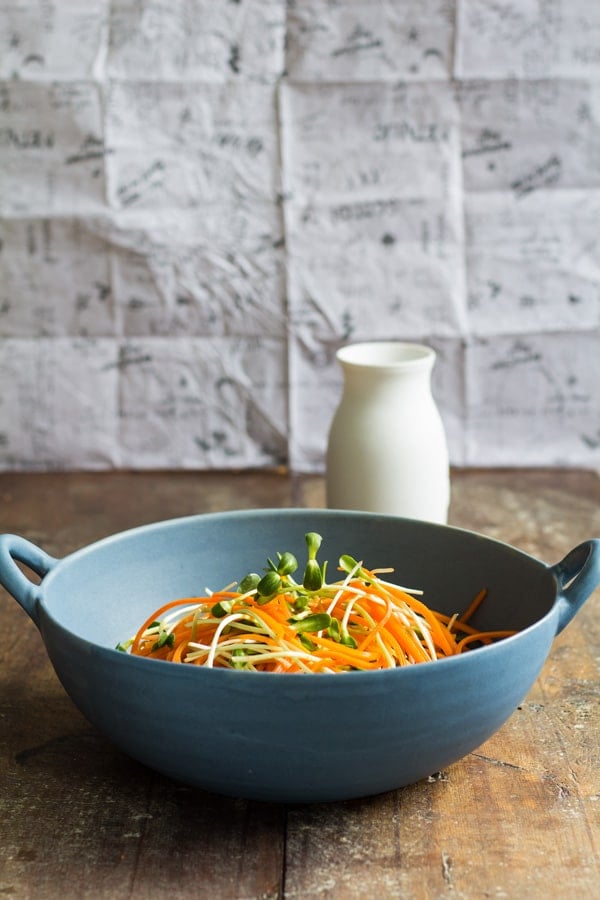 Sunflower Carrot Salad in a blue bowl with a white dressing jar in the background on a wooden board.