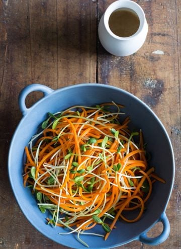 Top view of Sunflower Carrot Salad in a blue bowl with a white dressing jar on a wooden board.