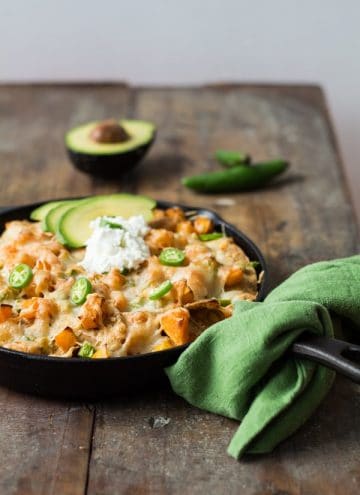 Butternut Squash Nachos in a black skillet with a green napkin on a wooden board.