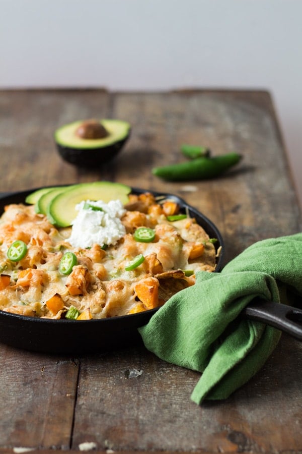 Butternut Squash Nachos in a black skillet with a green napkin on a wooden board.