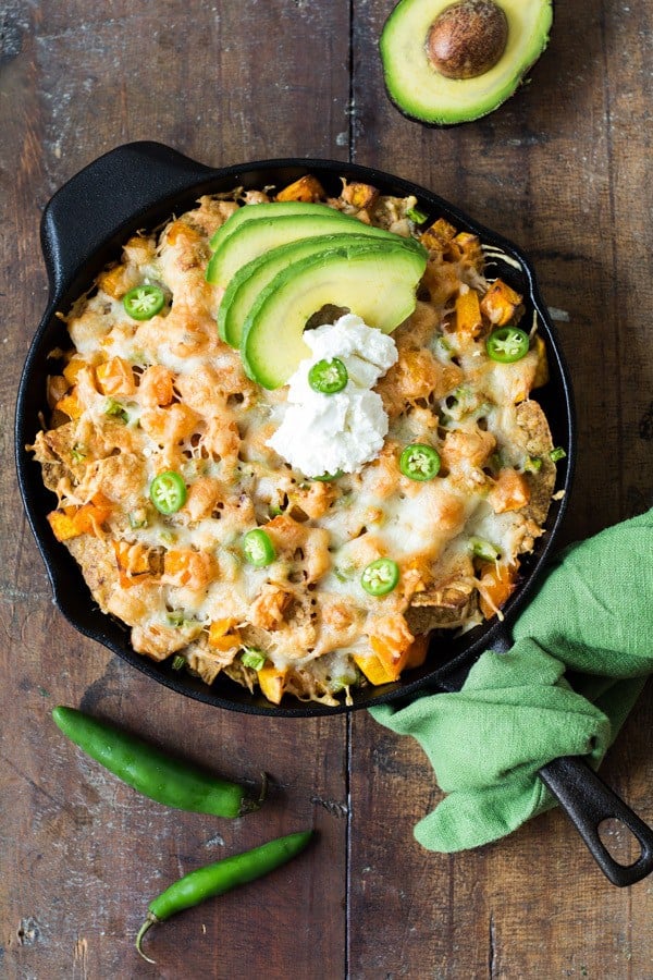 Top view of Butternut Squash Nachos in a black skillet garnished with sliced avocado on a wooden board.