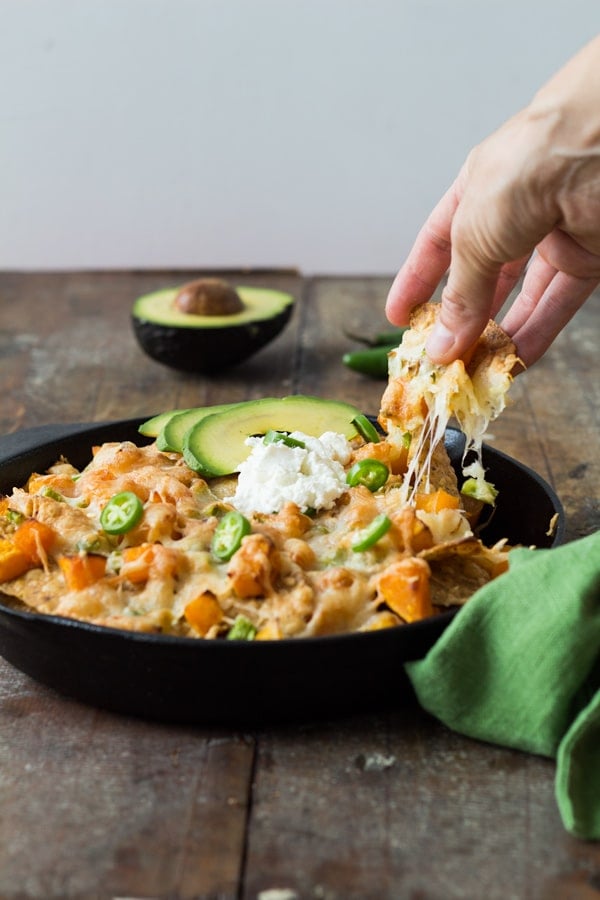 Hand grabbing a piece of Butternut Squash Nachos from the skillet.