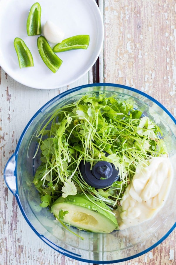 Ingredients for cilantro lime salsa in a food processor and a plate of sliced green chiles.