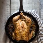 Easy Roast Chicken in skillet with a striped napkin underneath on a rustic wood board.