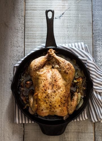 Easy Roast Chicken in skillet with a striped napkin underneath on a rustic wood board.