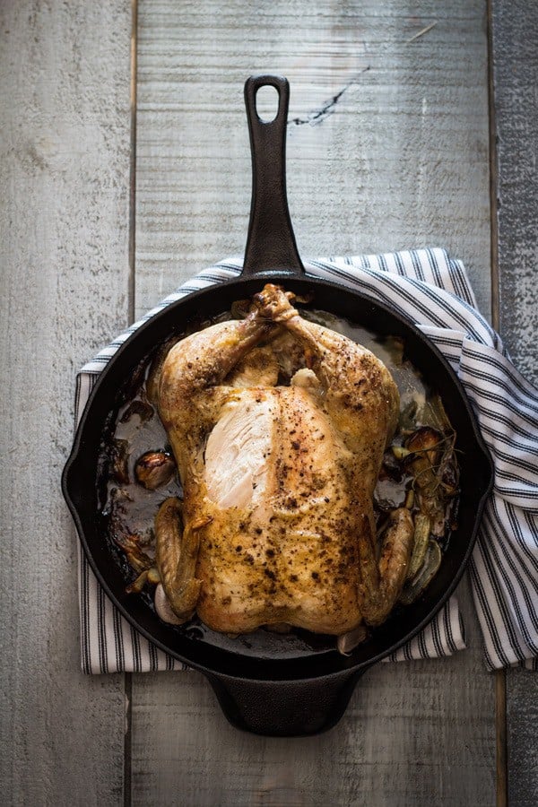 Easy Roast Chicken in skillet with a striped napkin underneath on a rustic wood board.