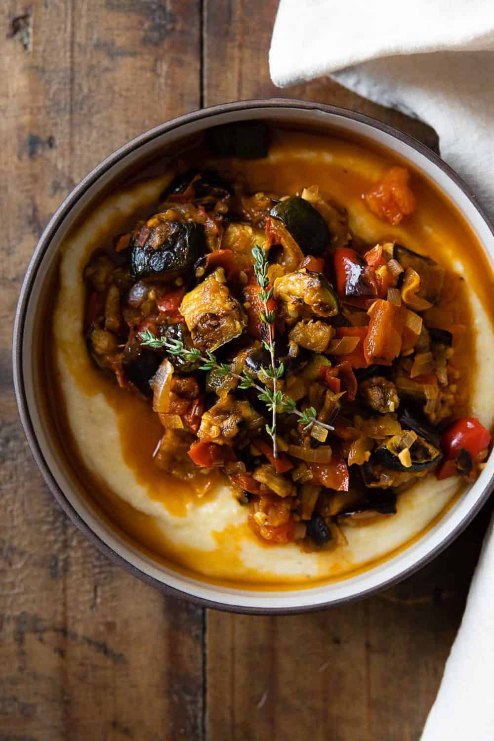 Ratatouille on polenta in a bowl on a wooden table.