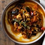 Ratatouille on polenta in a bowl on a wooden table.