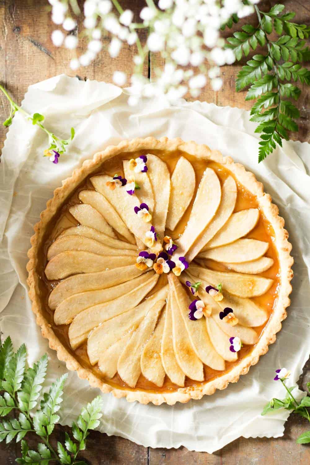 Top view of Simple Pear Tart on a white napkin and some flowers.