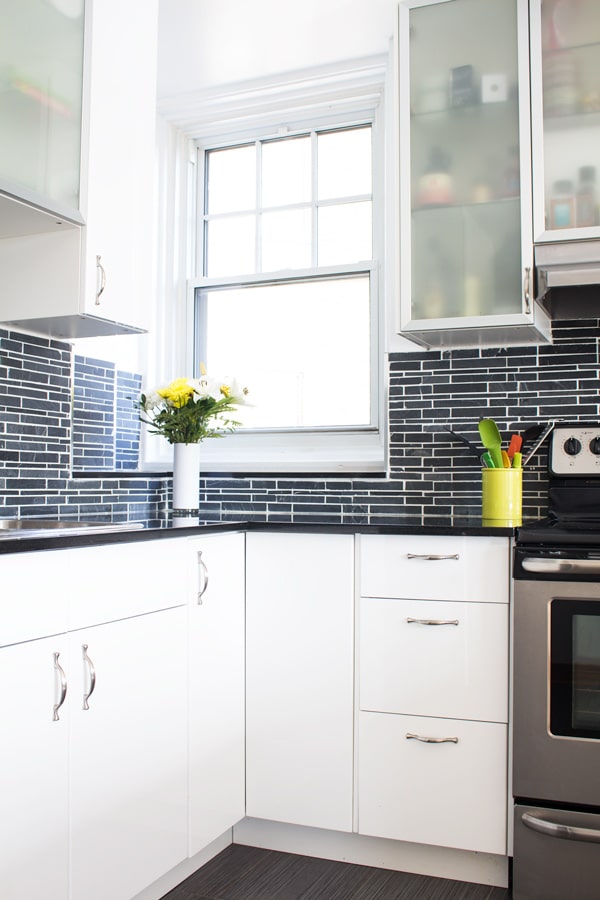 Corner of the New Kitchen of Green Healthy Cooking. White cabinets with black backsplash and flowers on the counter.