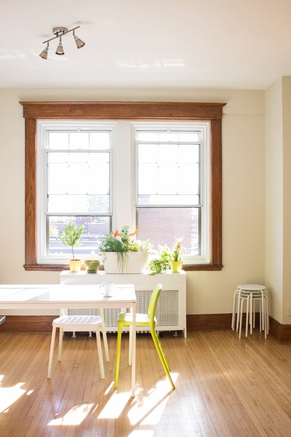 Part of a white dining table with two chairs, hardwood floors and big window in the background.