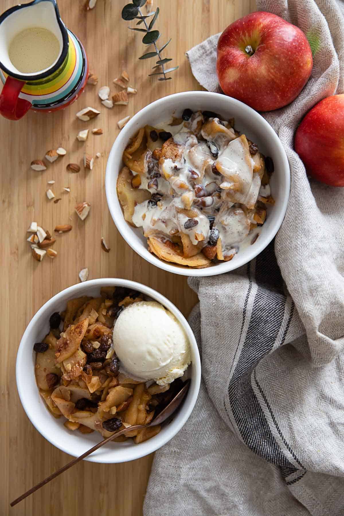 Two bowls of sliced baked apples one topped with custard the other topped with a scoop of vanilla ice cream.