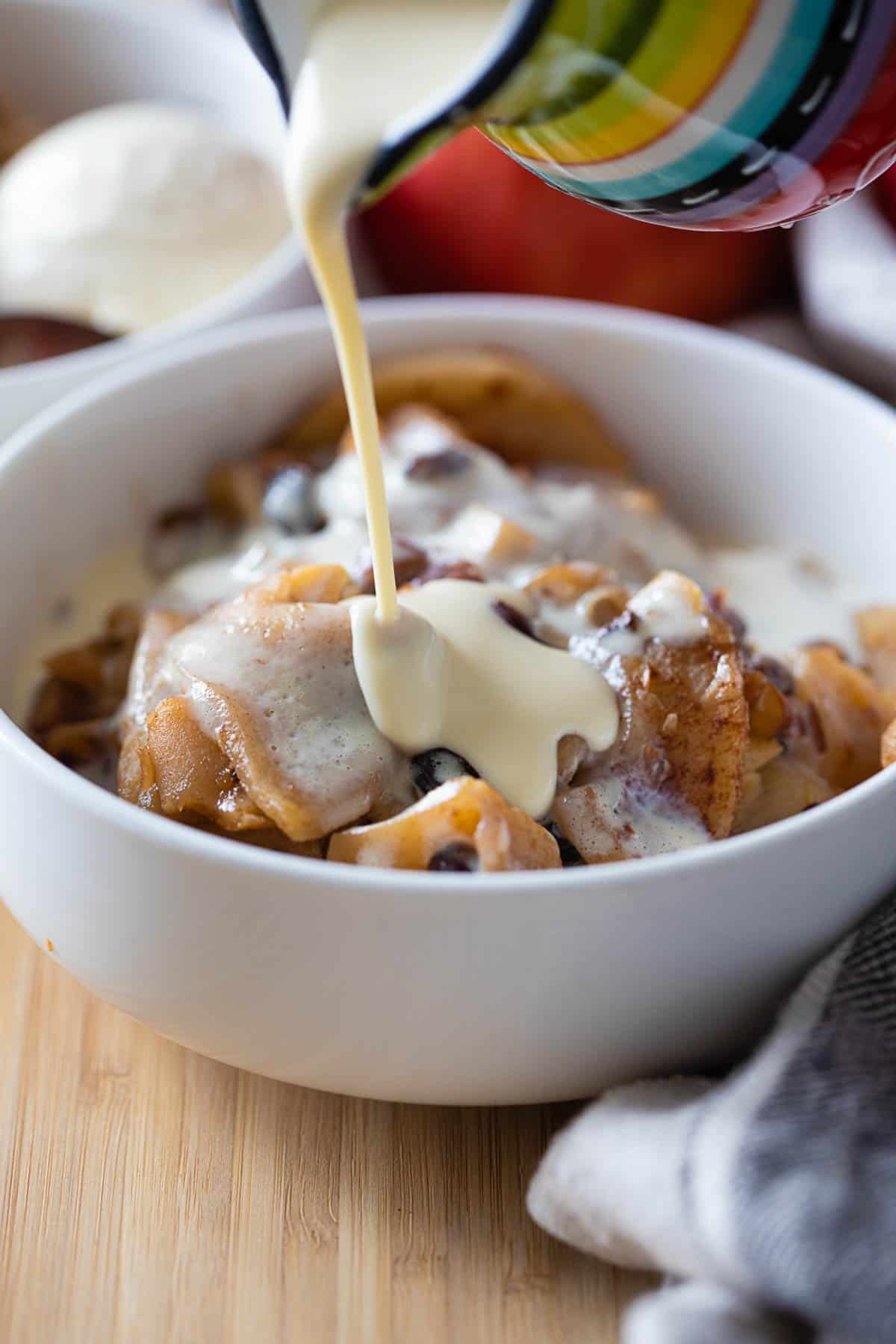 Vanilla custard being poured over sliced baked apples in a bowl.