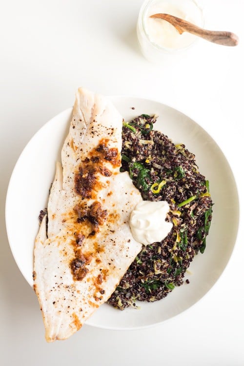 Top view of Haddock with Black Quinoa Risotto and creme fraiche on a white plate, and a cup with creme fraiche with a wooden spoon.