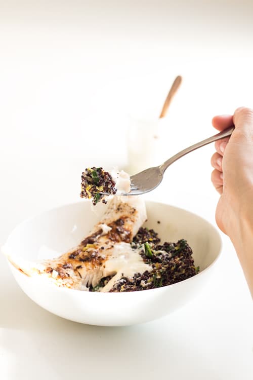A bowl of Haddock and Black Quinoa Risotto and a hand holding a fork with a bit of haddock and quinoa.