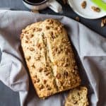 Top view of sliced Banana Bread with Maple Candied Walnuts, a cup of coffee, and an empty plate with a knife.