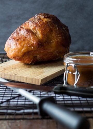 Baked Maple Mustard Ham on a wooden board and a jar of gravy.