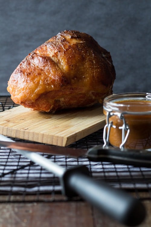 Baked Maple Mustard Ham on a wooden board and a jar of gravy.