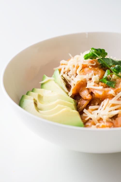 Close up of a bowl of Mexican Breakfast Chilaquiles con Camarones with shredded cheese and avocado slices.