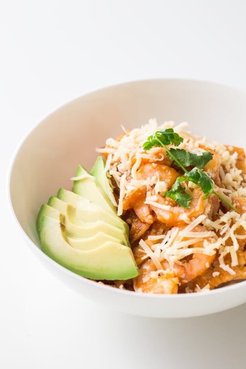 Close up of a bowl of Mexican Breakfast Chilaquiles con Camarones with shredded cheese and avocado slices.