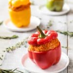 Close up of red Bulgur Stuffed Bell Pepper on a plate. Yellow and green peppers in the background.