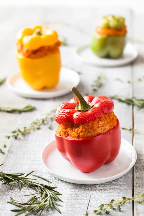 Close up of red Bulgur Stuffed Bell Pepper on a plate. Yellow and green peppers in the background.